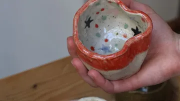 Hand hält bunte Keramiktasse drinnen.