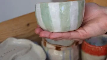 Hand holding a striped ceramic bowl indoors.