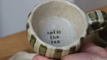Keramikbecher mit Text 'spill the tea'.