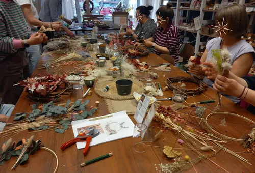 Personen machen Blumenkränze auf Holztisch.