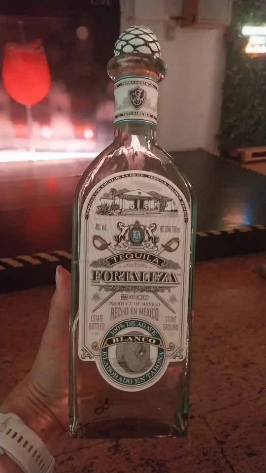 Tequila-Flasche in Hand gehalten, Bar-Hintergrund.
