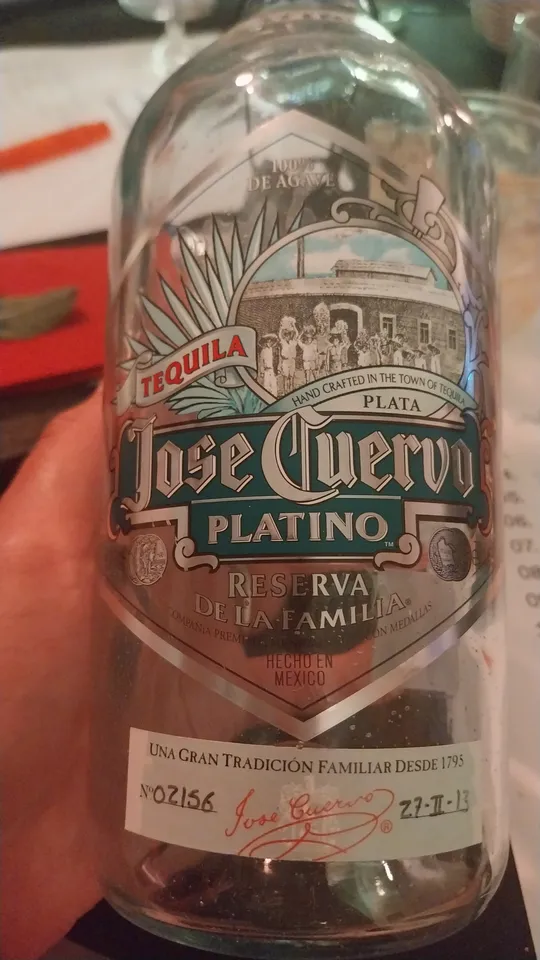 Tequilaflasche auf Tisch, roter Hintergrund.