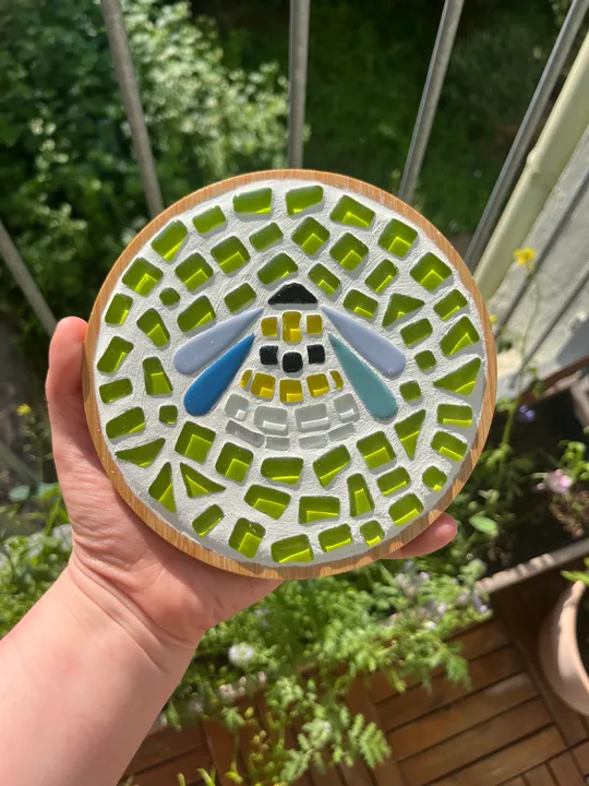Hand hält Mosaik-Bienendesign im Freien.