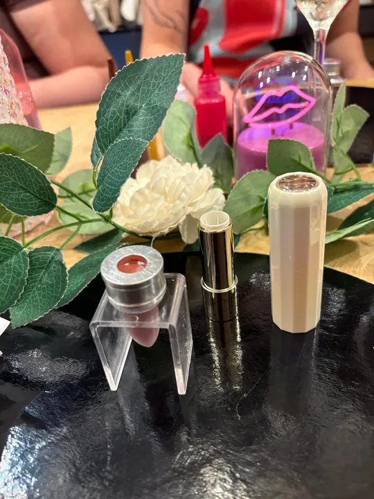 Lipstick tubes on black surface, surrounded by leaves.