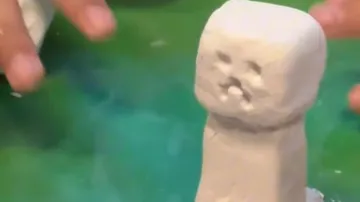 Tonfigur, geformt von Händen auf grüner Fläche.
