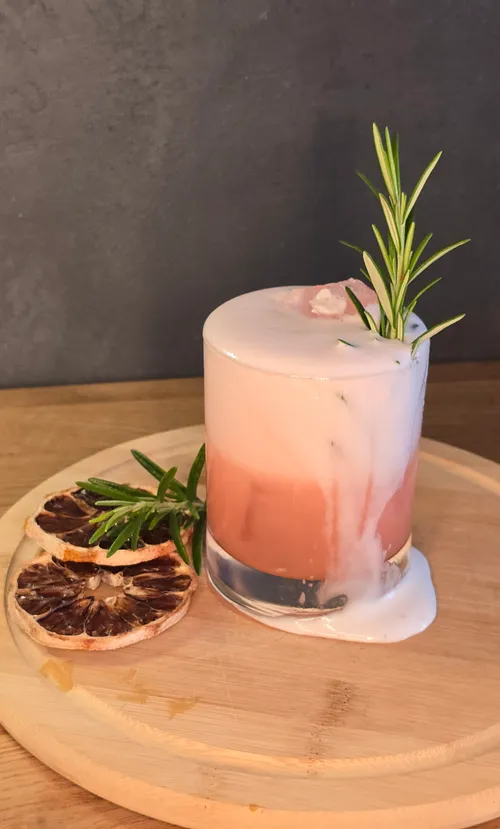Cocktail with foam on round wooden board.