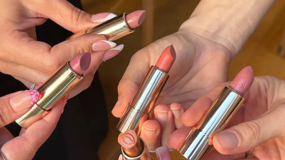 Fünf Hände halten verschiedene Lippenstiftfarben.