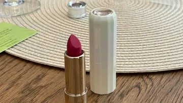 Lippenstift steht auf Holztisch neben Platzdeckchen.