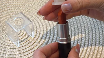 Hands hold lipstick on textured surface.