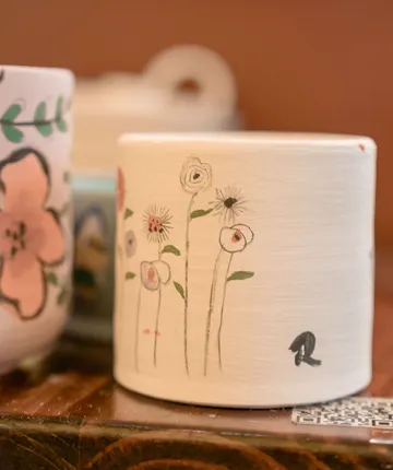 Dekorative Tassen mit Blumenillustrationen im Regal.