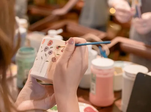 Person malt Blumen auf Keramiktasse.