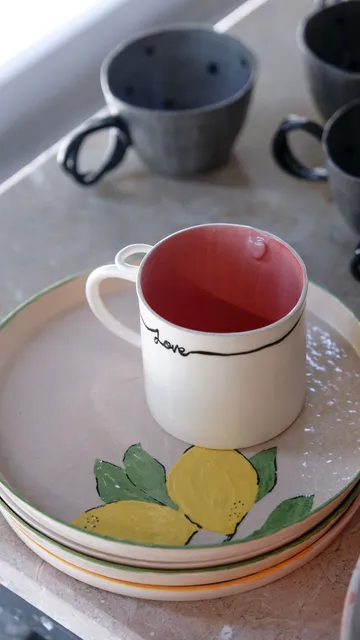 Ceramic cup on lemon-patterned plate, table setting.