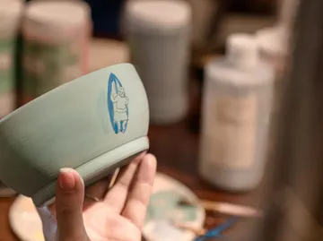 Hand hält bemalte Schüssel in Werkstatt.