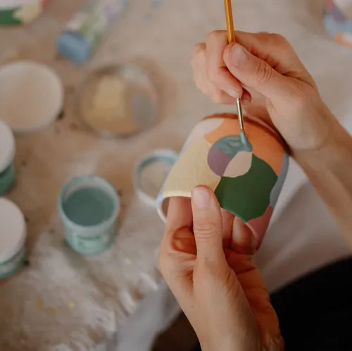 Hände bemalen bunte Keramiktasse drinnen.