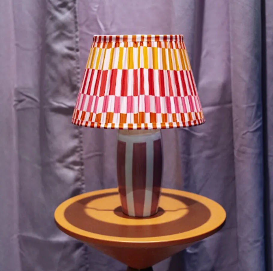 Striped lamp sits on round wooden table.