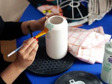 Hände bemalen weiße Vase auf Tisch.