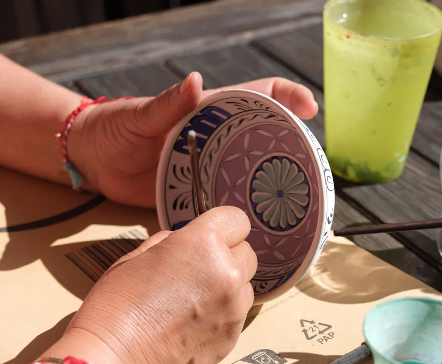 Hands painting ceramic plate outdoors.