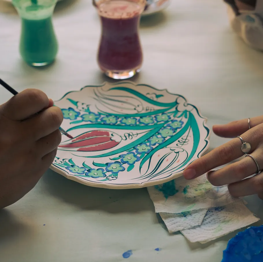 Hands painting a decorative plate indoors.