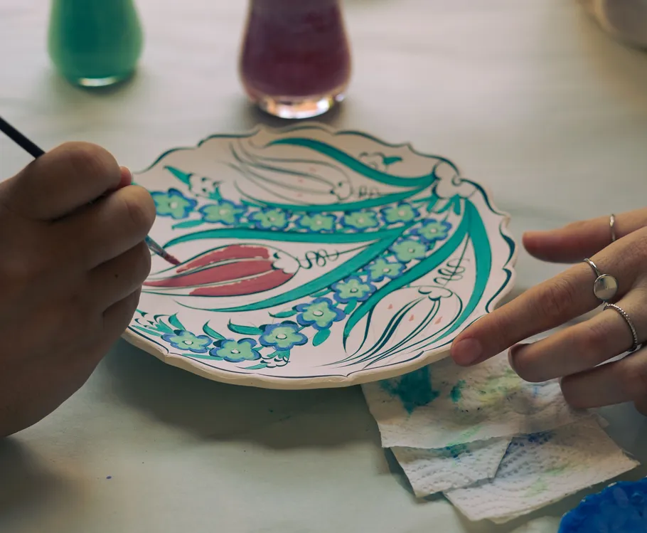 Person painting floral plate on table.