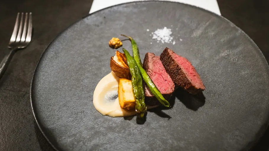 Gourmet steak with vegetables on dark plate.