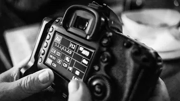 Camera screen with settings displayed, held by hands.