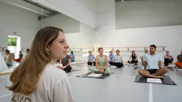 Menschen sitzen im Schneidersitz im Yoga-Studio.