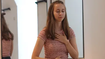 Woman holding chest, eyes closed, indoors.