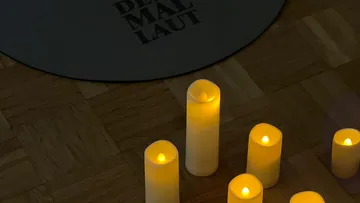 Candles glowing on wooden floor, carpet nearby.