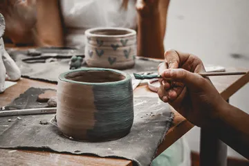 Hand paints pottery on table surface.