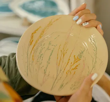 Plate with floral designs held by hands.
