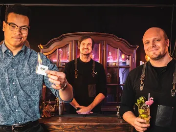 Drei Barkeeper in einer Bar zeigen einen brennenden Gegenstand.