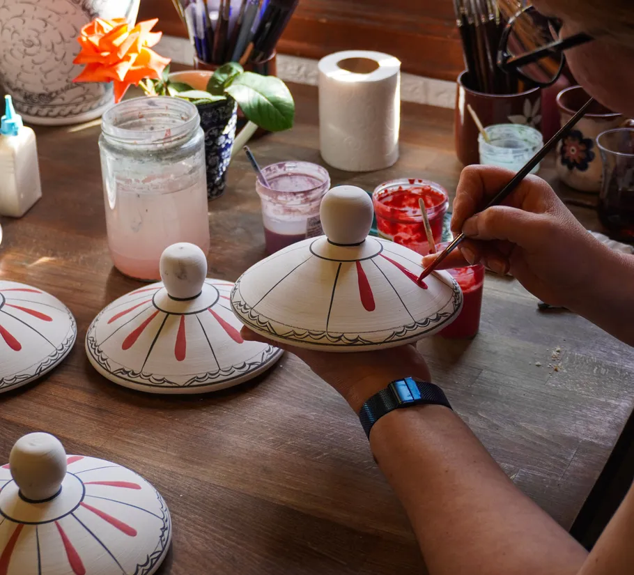 Person painting ceramic lids at a workshop.