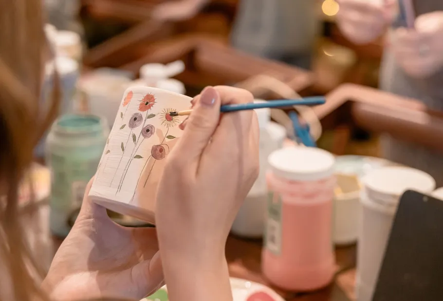 Person painting ceramic pot with flowers.