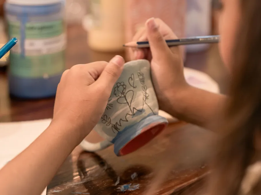 Child drawing on a ceramic cup.