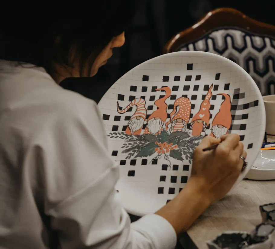 Person painting gnomes on a plate indoors.