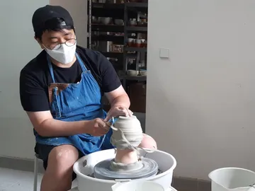 Potter forms clay on a potter's wheel in a workshop.