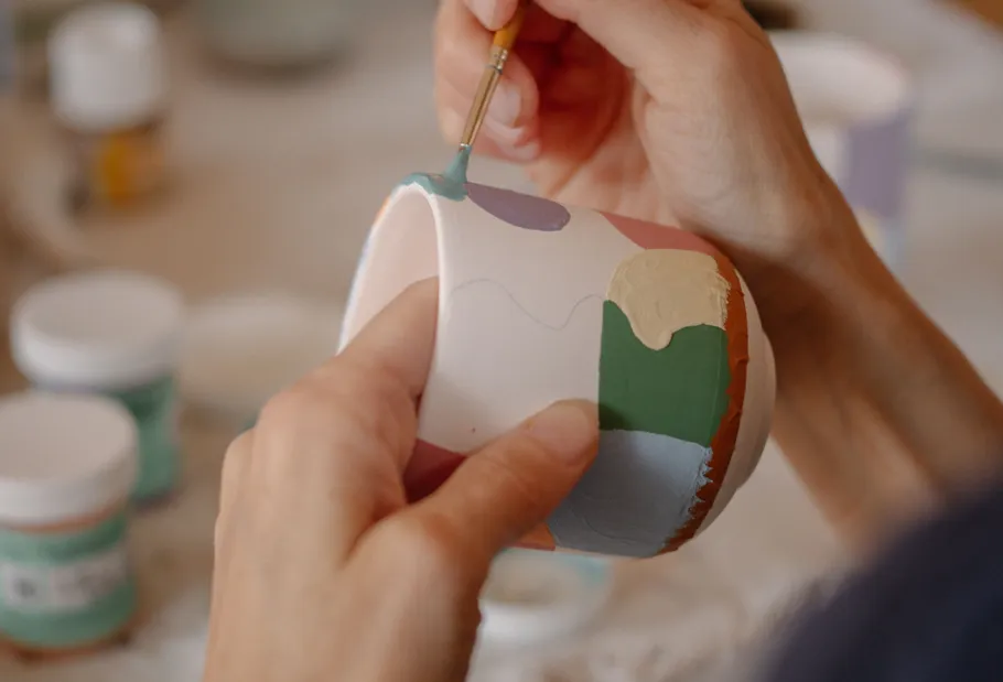 Person painting multicolored cup indoors.