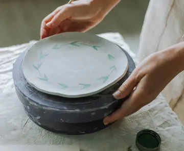 Hands painting ceramic plate on table.
