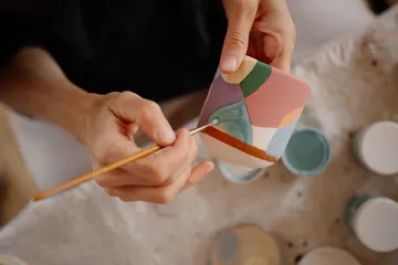 Hand paints colorful abstract pattern on ceramic.