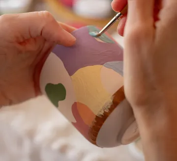 Hände bemalen bunte Keramiktasse.