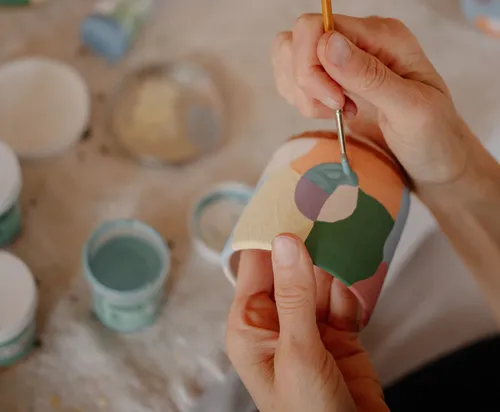 Hände bemalen bunte Keramik drinnen.