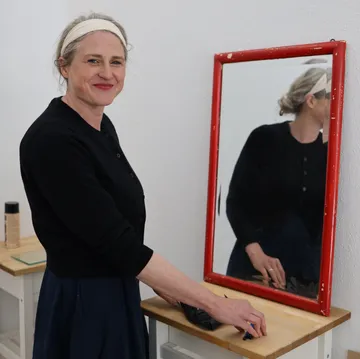 Frau steht am Spiegel, lächelt drinnen.