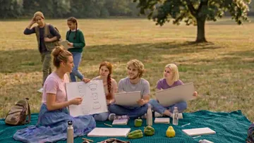 People sketching outside on a picnic blanket.