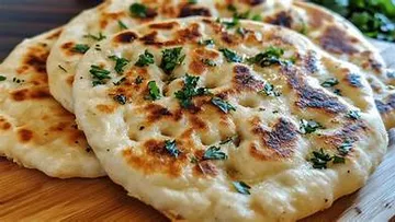 Flatbreads with herbs on wooden board.