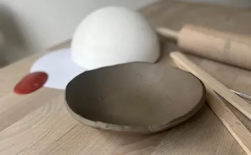 Clay bowl on wooden table with tools.