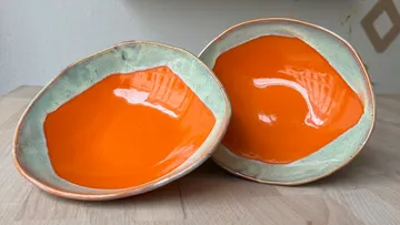 Two orange bowls on wooden surface.