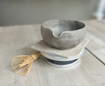 Clay bowl and whisk on wooden table.