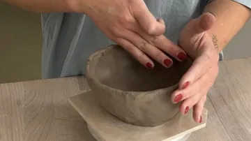 Hände formen Tonschüssel auf Tisch.