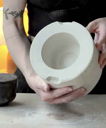 Person holding white ceramic mold indoors.