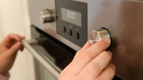 Hand adjusting oven dial in kitchen.